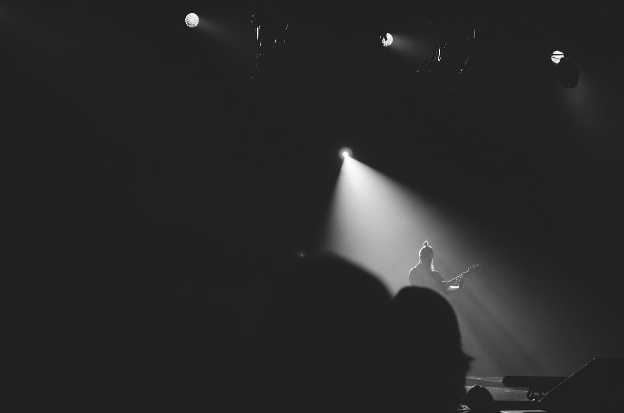 a black and white photo of a person on stage, by Matija Jama, unsplash, light and space, playing guitar onstage, spotlight from above, subtle fog and mood lighting, vsco film grain