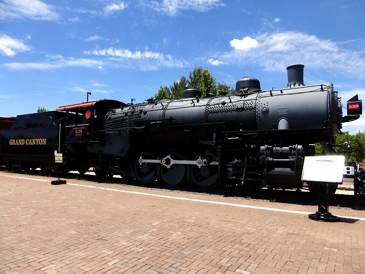 a large black train sitting on top of a train track, at the museum, albuquerque, white steam on the side, looking from side and bottom!