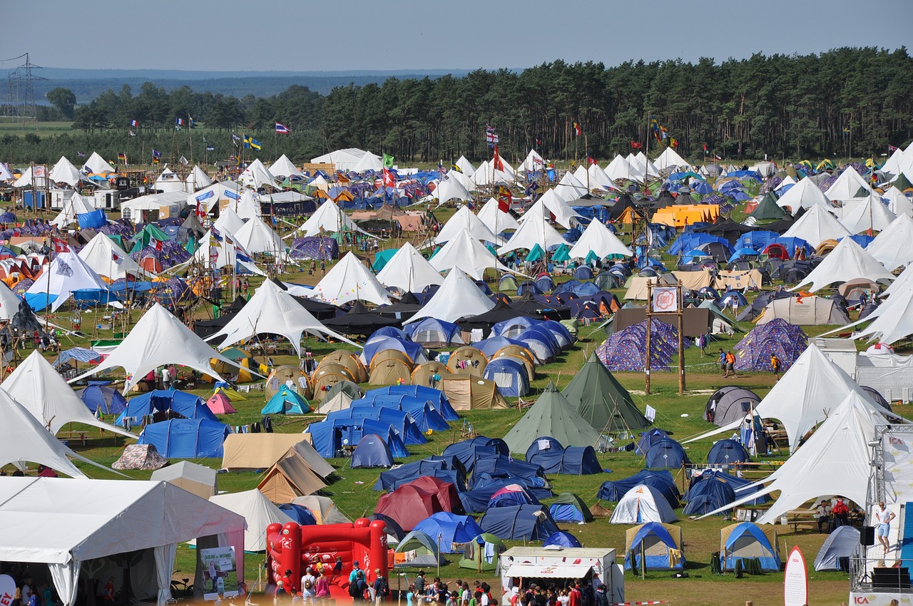 a large group of tents sitting on top of a lush green field, a photo, by Dave Allsop, maximalism, open plan, in 2 0 1 2, camp half-blood, overview