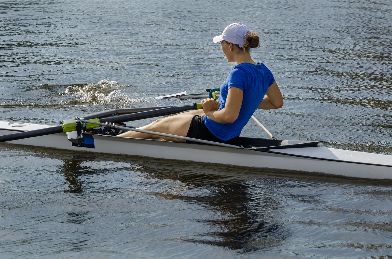 a woman sitting on top of a boat in the water, by Alison Debenham, shutterstock, purism, in a race competition, sculls, profile close-up view, on a riverbank