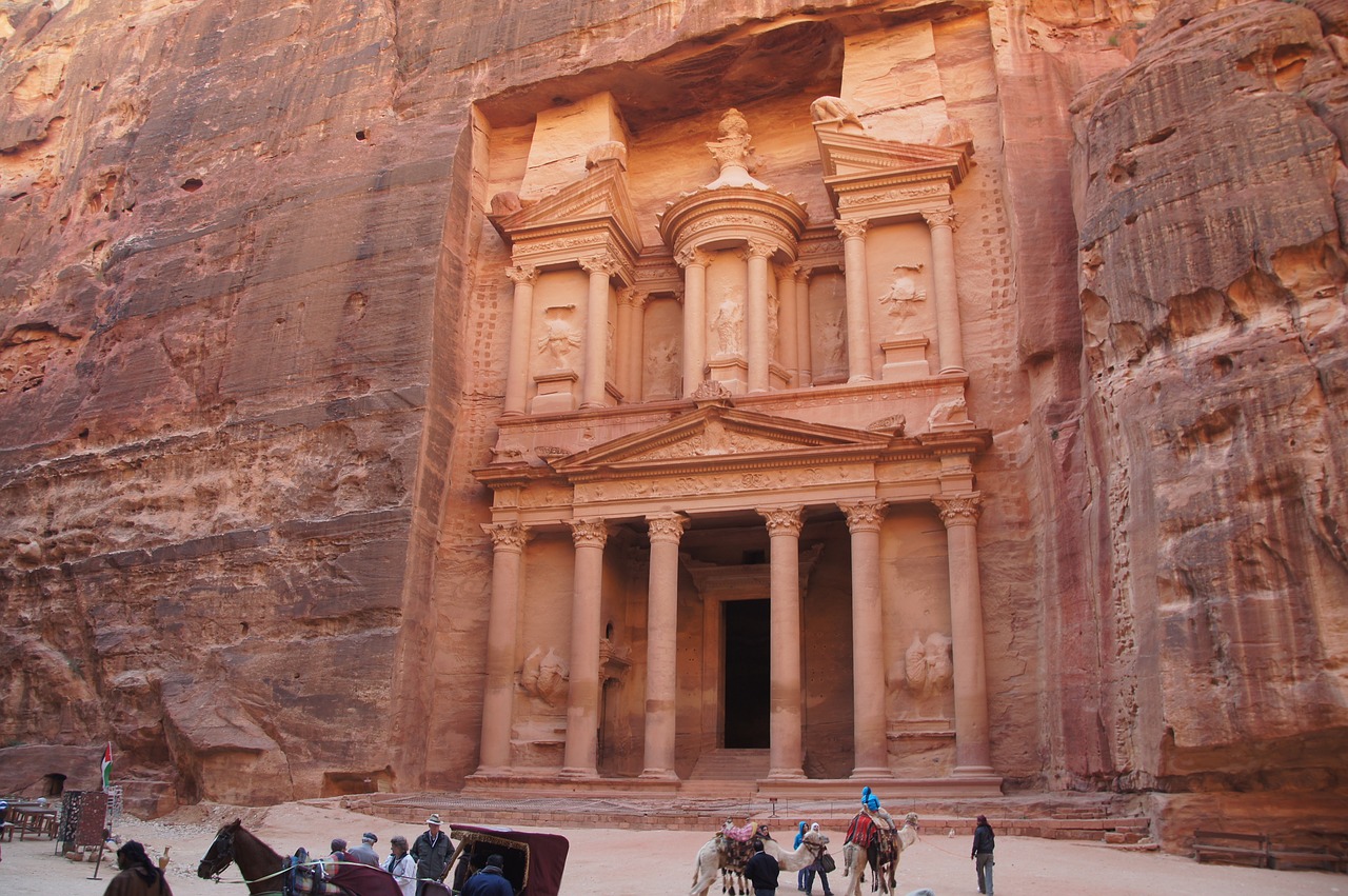 a group of people riding horses in front of a building, a picture, red sandstone natural sculptures, gigantic pillars, ancient monument waterfall, carved stone