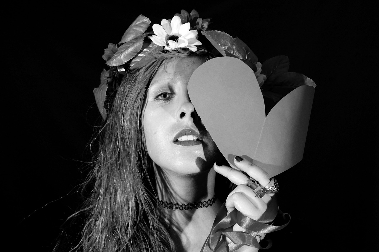 a woman holding a paper heart in front of her face, a black and white photo, inspired by Grete Stern, renaissance, 1 9 8 0 s flower power hippy, ellie bamber fairy, chiaroscuro!!, shot on nikon z9