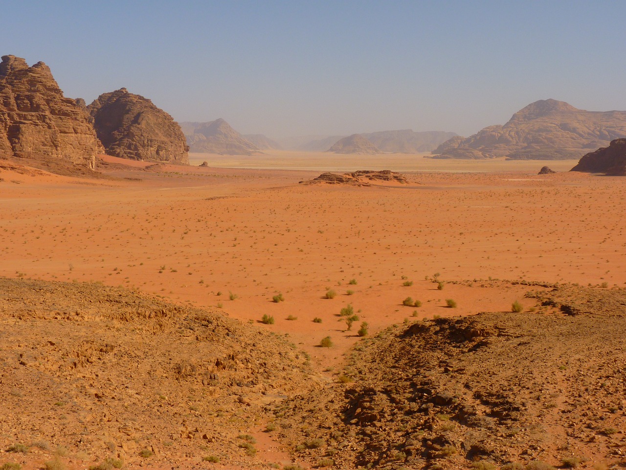 a person riding a horse in the middle of a desert, hurufiyya, landscape with red mountains, viewed from very far away, sparse vegetation, red sand