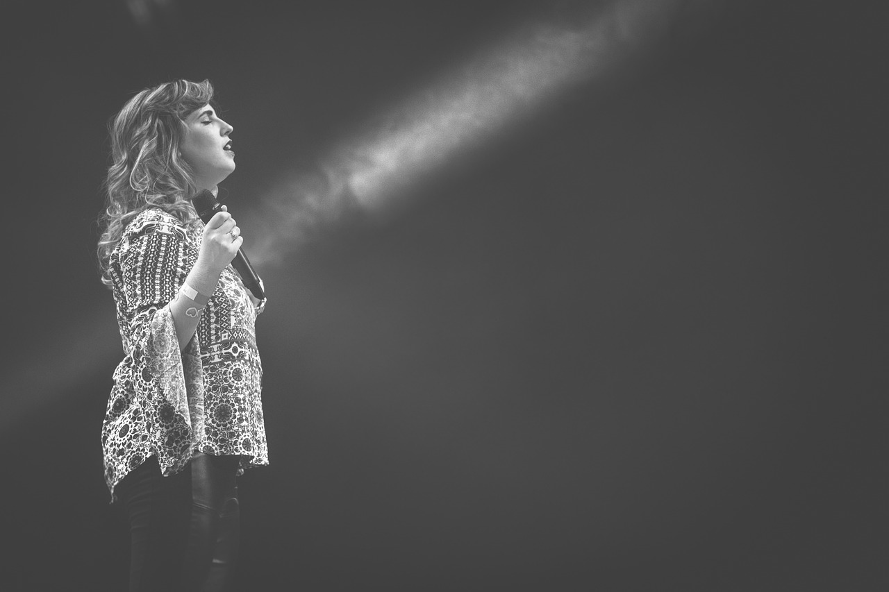 a black and white photo of a woman singing into a microphone, light and space, florence pugh, shot on sony alpha dslr-a300, stage photography, pointing to heaven