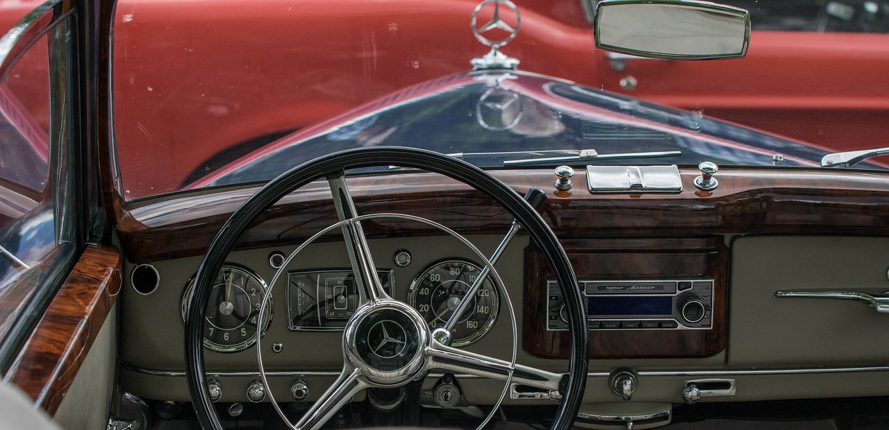 a close up of a steering wheel and dashboard of a car, by Hans Schwarz, unsplash, retrofuturism, mercedez benz, wine-red and grey trim, 1950s vibes, viewed through the cars window