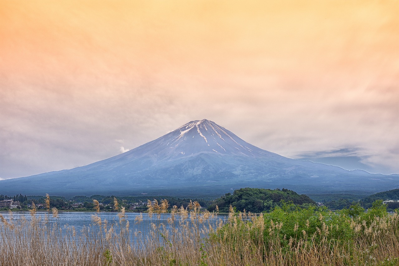 a large mountain towering over a body of water, a picture, by Kanō Tan'yū, shutterstock, fuji lut, grass mountain landscape, 1128x191 resolution, volcano landscape