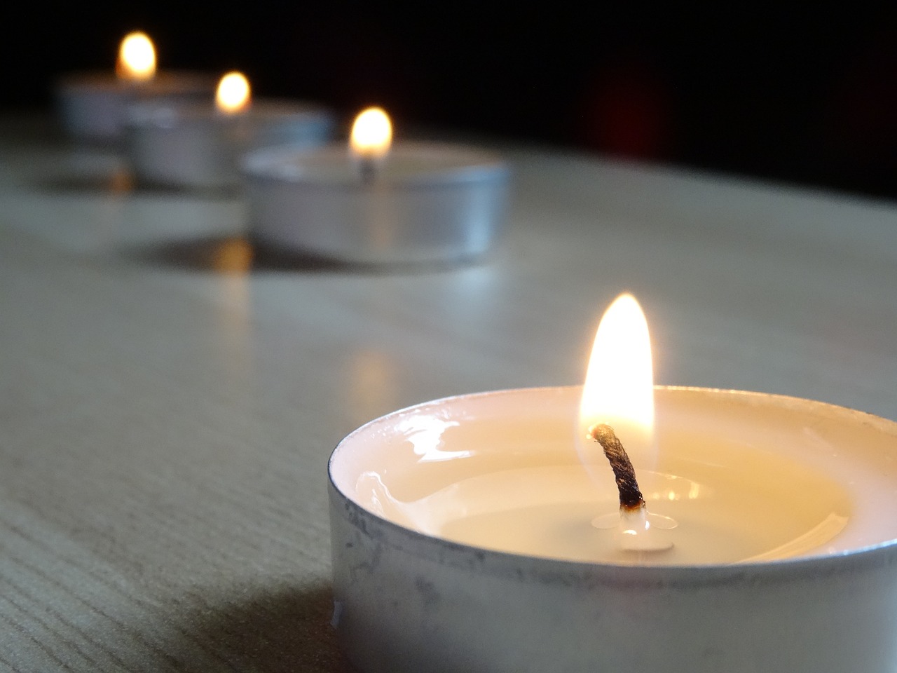 a group of lit candles sitting on top of a table, a picture, pixabay, minimalism, close up angle, half image, back towards camera, on a wooden desk