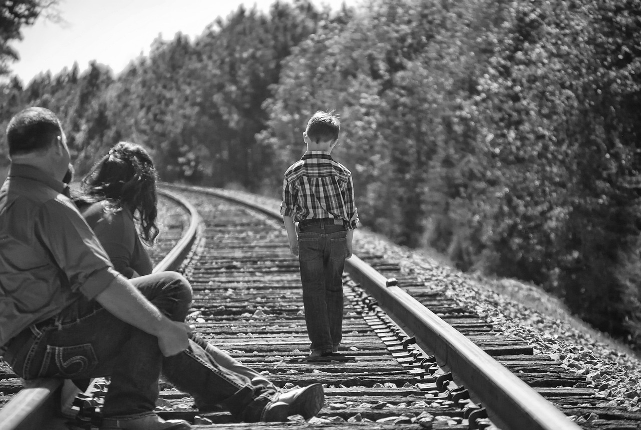 a couple of people sitting on a train track, a black and white photo, by Lucia Peka, pexels, fine art, little boy, standing with her back to us, husband wife and son, broken down