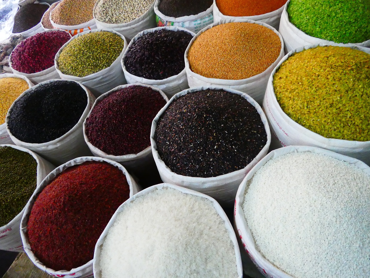 a table topped with lots of different types of rice, a photo, pexels, renaissance, colored market stand, sand particles, maroon, green