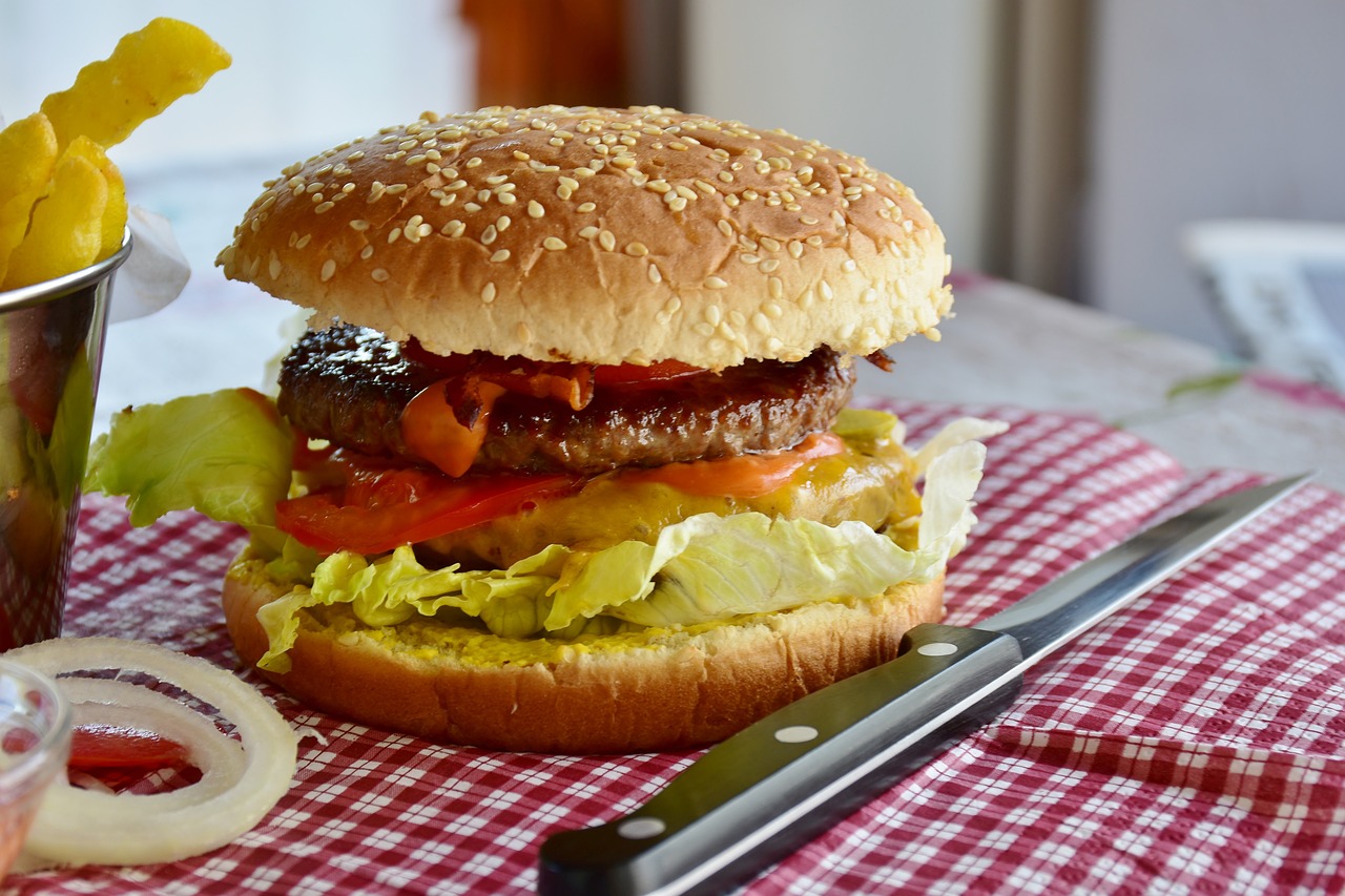 a hamburger sitting on top of a table next to a cup of fries, a picture, by Joe Bowler, pexels, realism, voluptuous sesame seed bun, extra onions and ketchup, avatar image, homemade