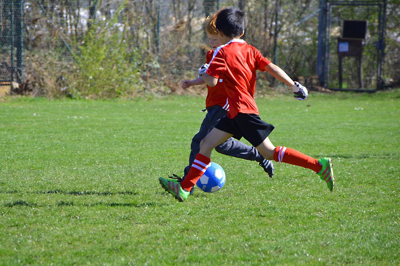 a young person kicking a soccer ball on a field, a picture, dribble, kids playing, sports photo, reds, springtime
