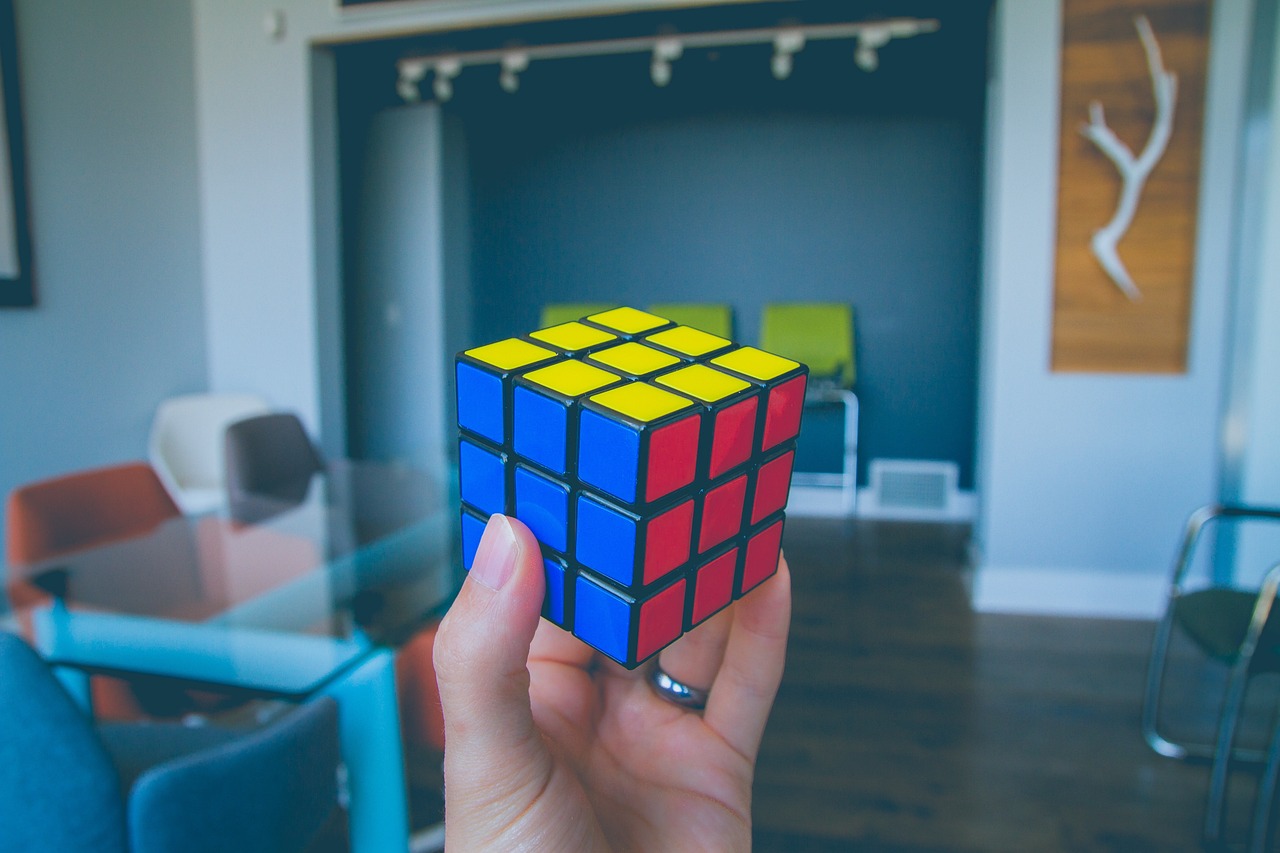 a person holding a rubik cube in their hand, inspired by Ernő Rubik, pexels, cubo-futurism, next to a window, in small room, red yellow blue, with a square