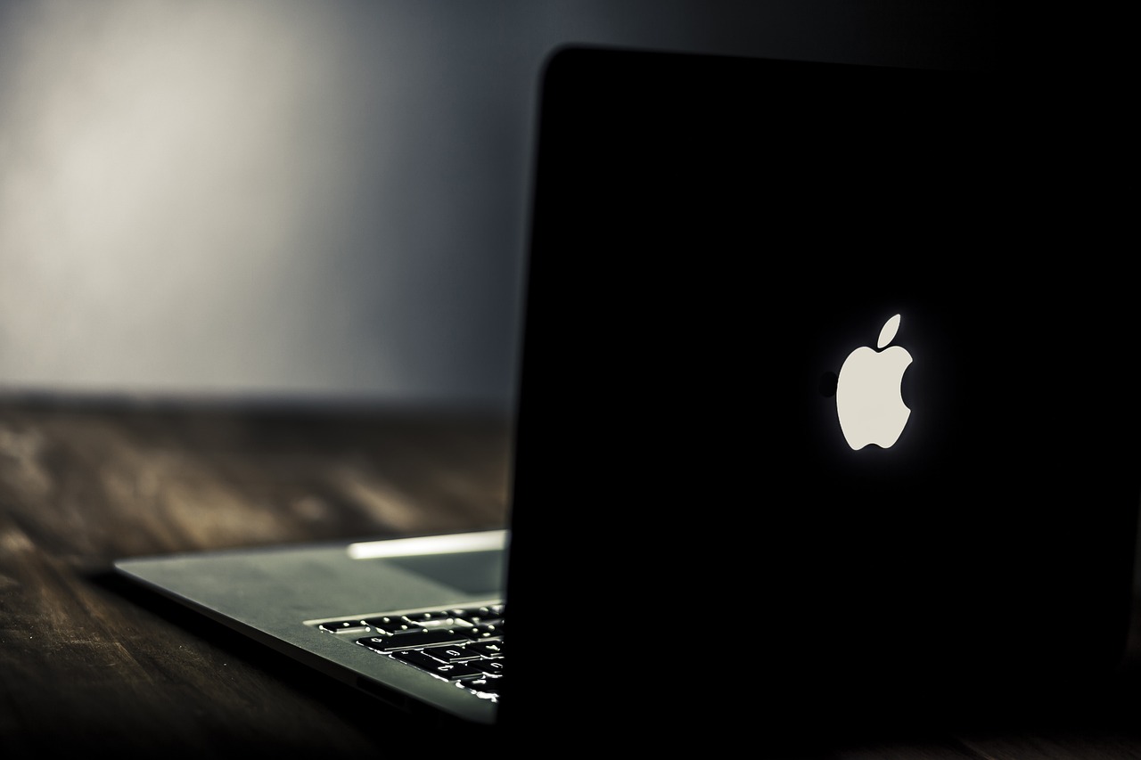 a laptop computer sitting on top of a wooden table, by Niko Henrichon, pexels, apple logo, back light, black velvet, rotating