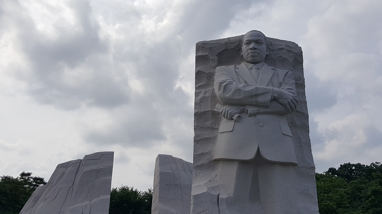 a statue of a man in a suit and tie, martin luther king, facing away from the camera, large stone statues of heroes, creating a thin monolith