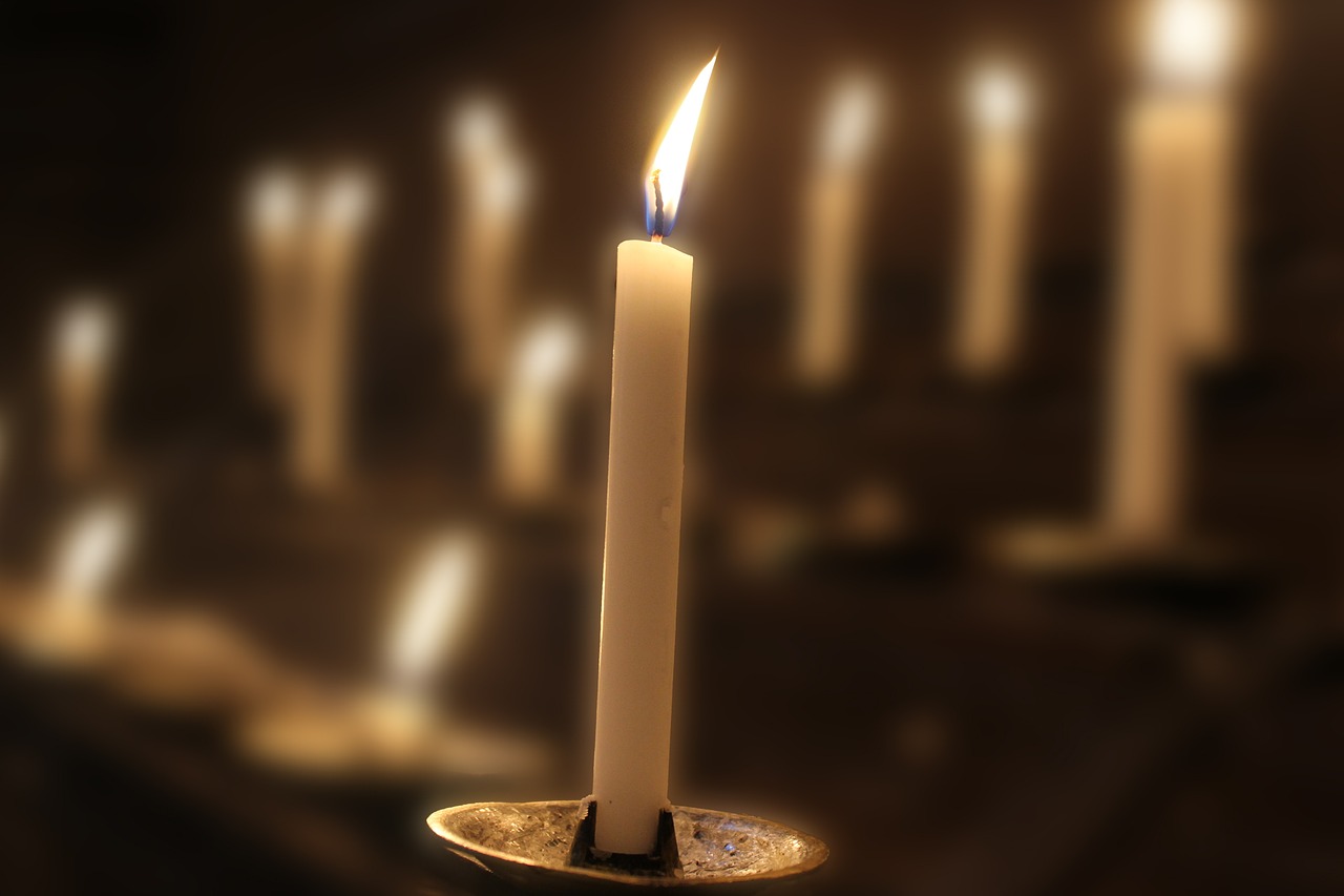 a lit candle sitting in front of a row of candles, a tilt shift photo, enhanced photo, high details photo, in a monestry natural lighting, raytraced lighting