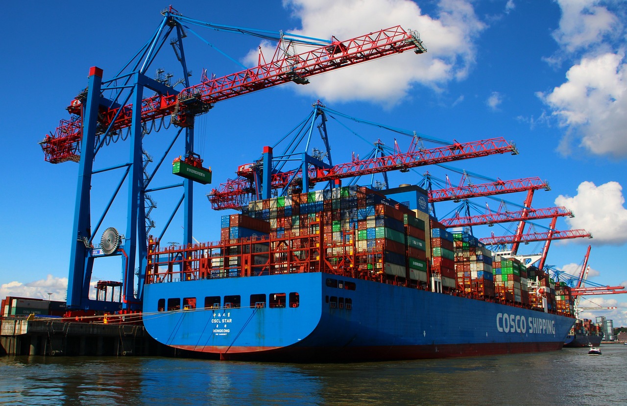 a large container ship sitting on top of a body of water, by Karl Völker, pexels, constructivism, blue and red color scheme, huge machine cranes, crypto, view from ground level