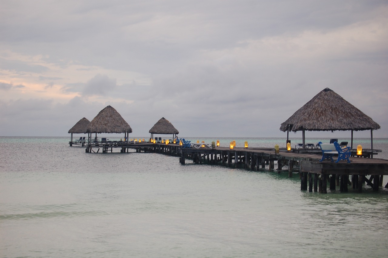 a group of people sitting on a pier next to the ocean, by William Thon, flickr, monsoon on tropical island, hotel, overcast dusk, maya