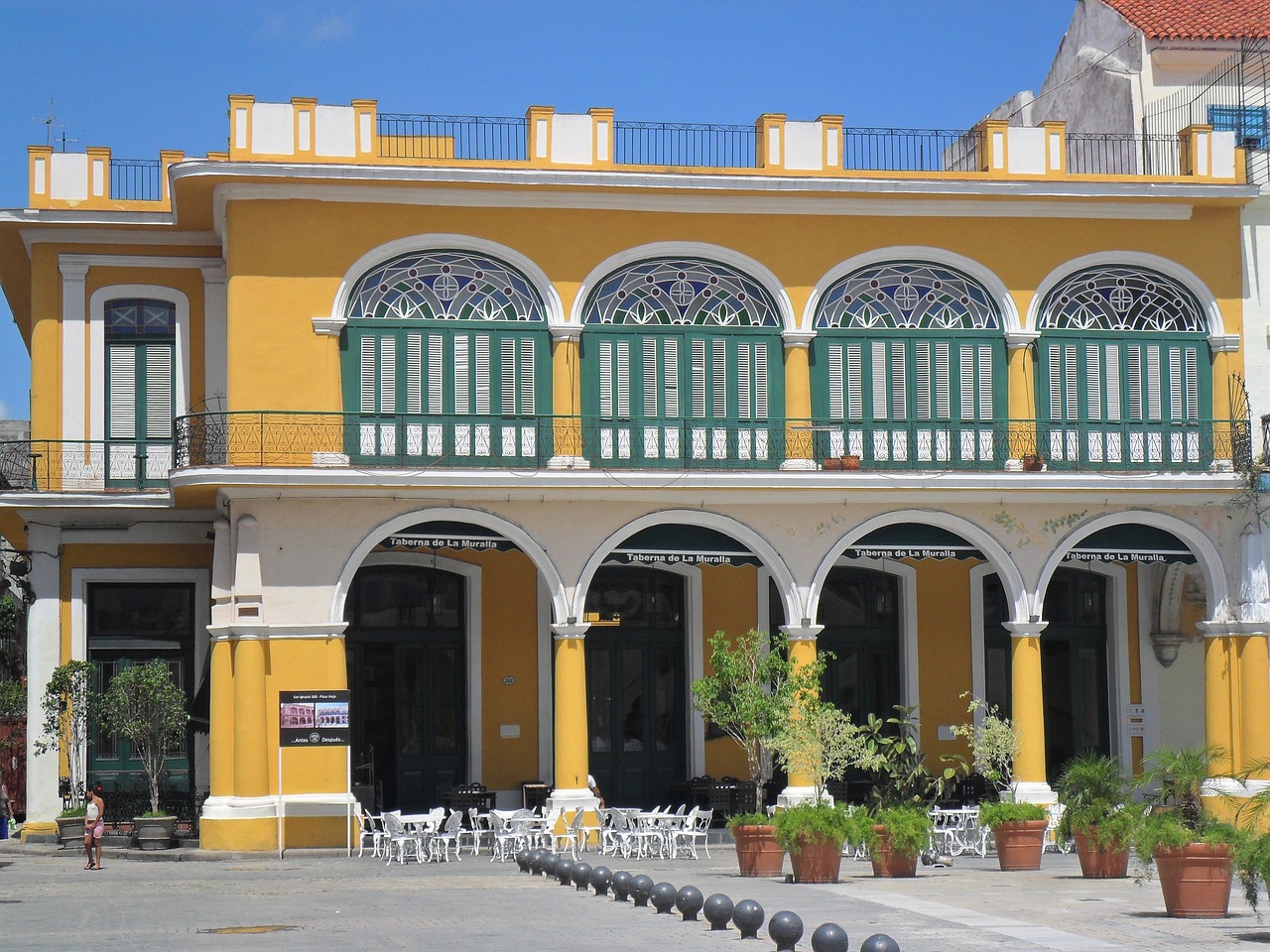 a row of tables and chairs in front of a yellow building, inspired by Ceferí Olivé, art nouveau, puerto rico, wikimedia commons, square, view from front