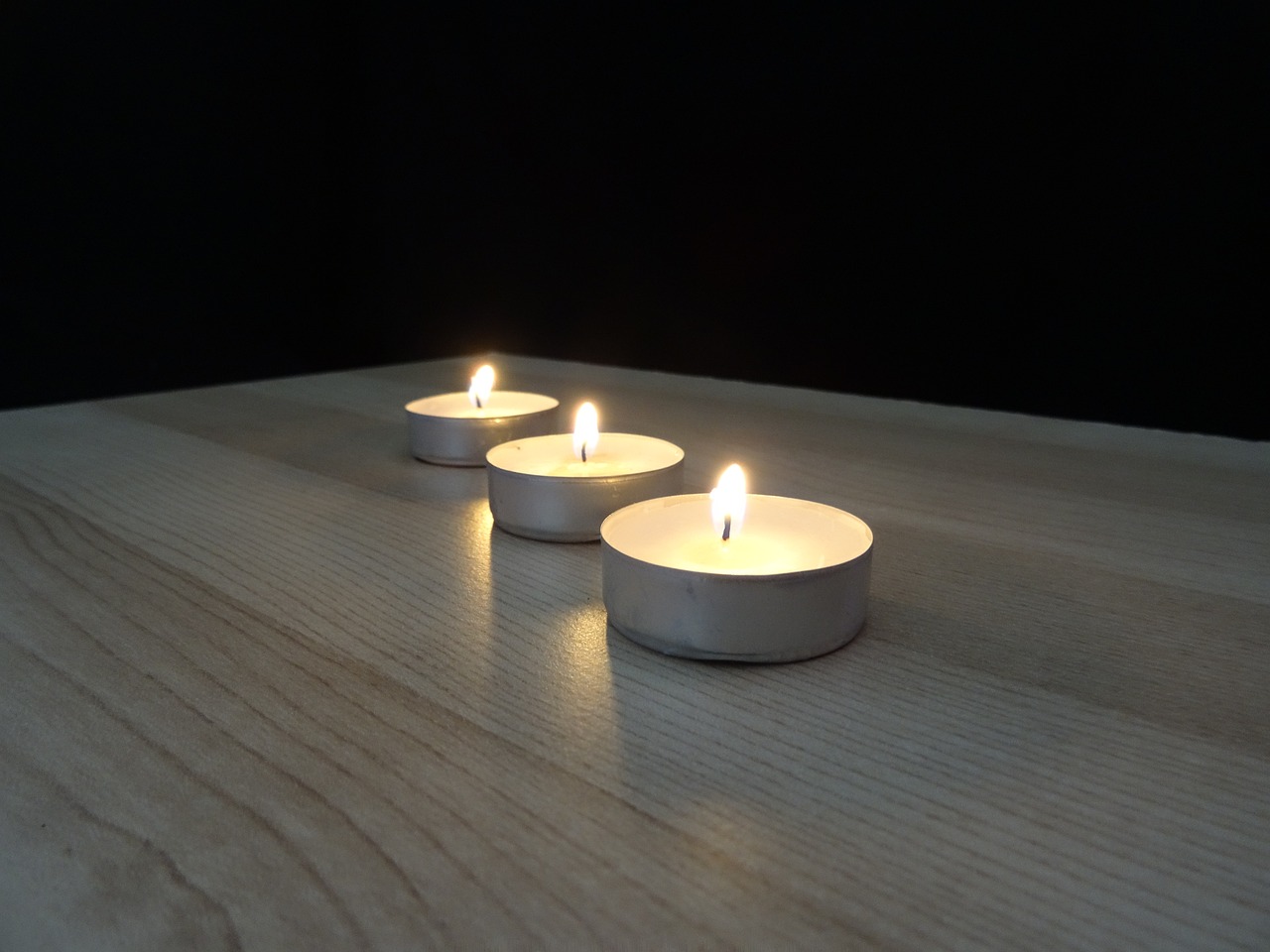 three lit candles sitting on top of a wooden table, above side view, photo 1 5 mm, zinc white, around 20 yo