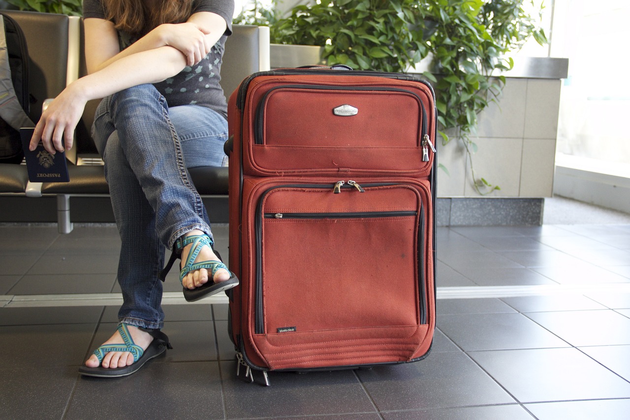 a woman sitting on a bench next to a red suitcase, istockphoto, crowded airport, new mexico, couple