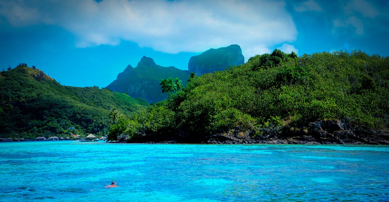 a person swimming in a body of water with mountains in the background, a picture, by Tom Wänerstrand, polynesian god, beautiful tropical island beach, greens and blues, blog-photo