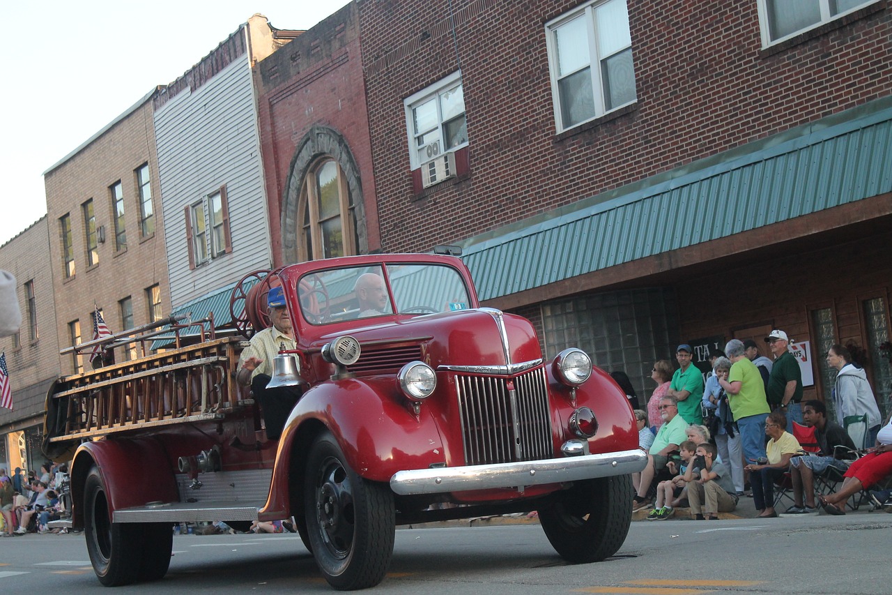 a red fire truck driving down a street next to a crowd, a photo, by Mike Bierek, flickr, folk art, ohio, beautiful lady, old car, 2 0 1 0 photo