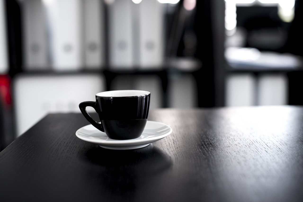 a coffee cup sitting on top of a wooden table, a tilt shift photo, by Karl Buesgen, black lacquer, office background, black an white, server