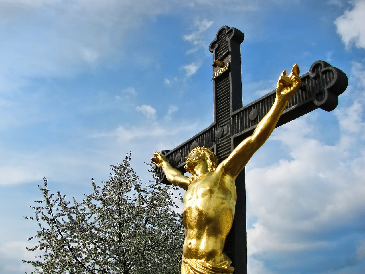 a golden statue holding a cross standing in front of a tree