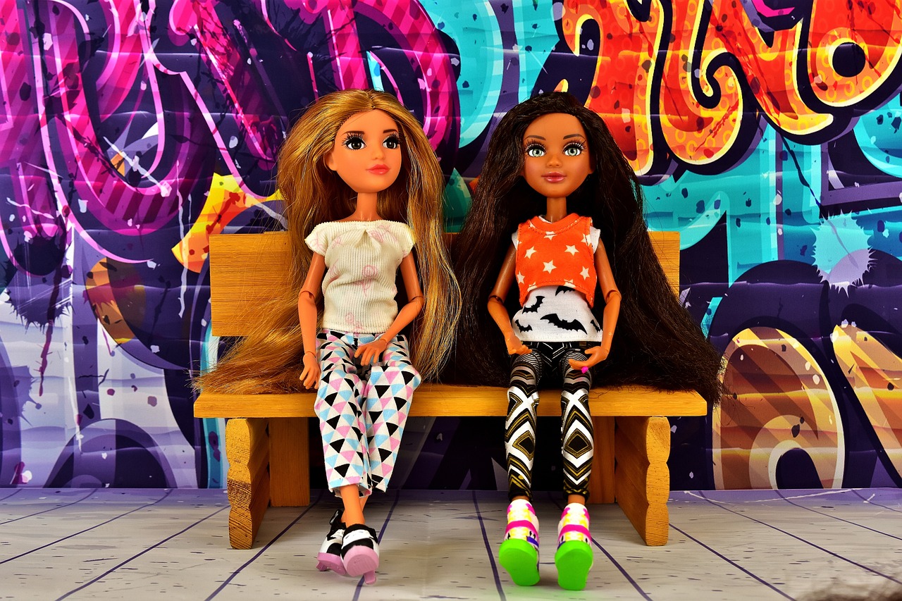 two dolls sitting on a bench in front of graffiti
