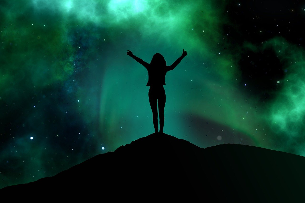 the woman is standing on a hilltop and arms wide open