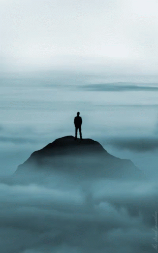 a man stands on top of a mountain overlooking the cloudy sky