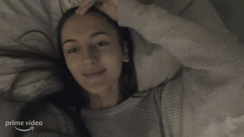a woman smiles behind the covers in a bed