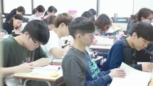 students are sitting in desks with one writing on a piece of paper