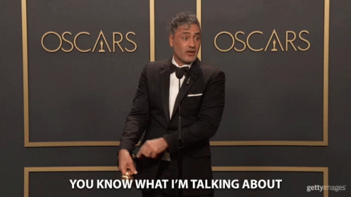 a man in a tuxedo standing in front of a oscars sign