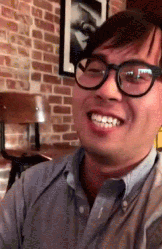 a man in glasses is laughing in a room with a blue brick wall