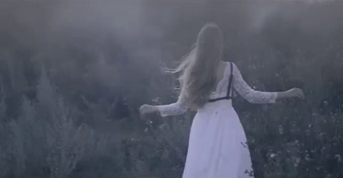 a woman is standing in a field of grass and fog