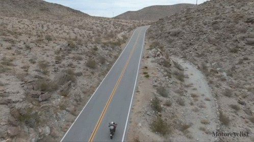 two motorcycles riding on an empty road in the desert