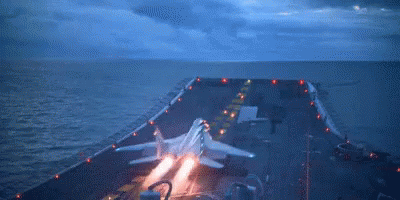 an aircraft carrier with lights is landing at night
