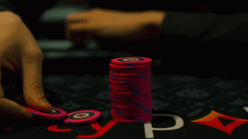 two hands grabbing up purple chips on top of a card game table