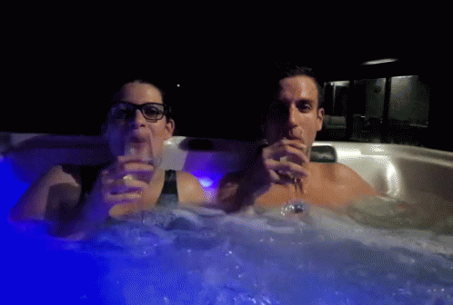 two people holding beverages are in the bathtub