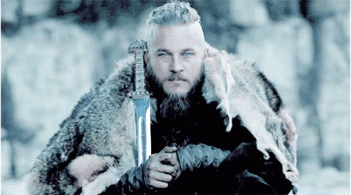 a man in winter clothes holds a sword and looks at the camera