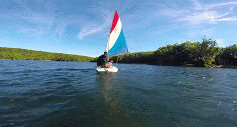 man sails on calm lake under beautiful sky
