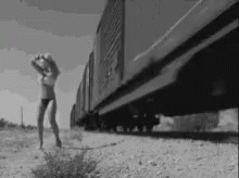 the girl standing on the side of the road is looking at the train