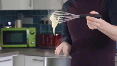 someone in white gloves holds a whisk as they whisk soing out of a pot