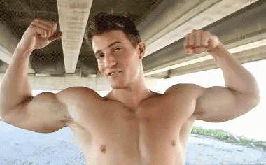 shirtless man posing in front of underpass with hands raised