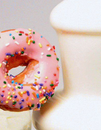 a purple frosted donut with sprinkles in front of a glass
