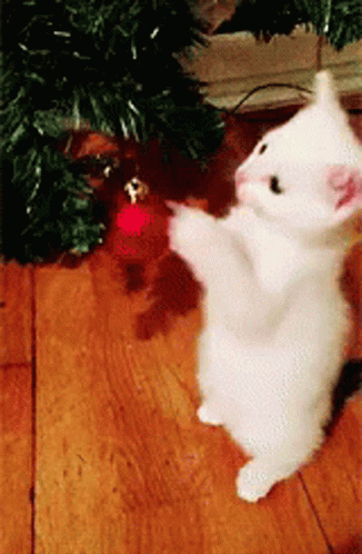 a white stuffed animal sitting on the ground in front of a christmas tree