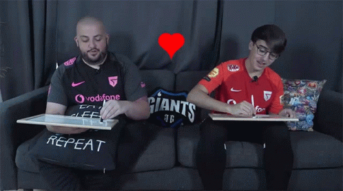 two men sitting on a couch with one man signing