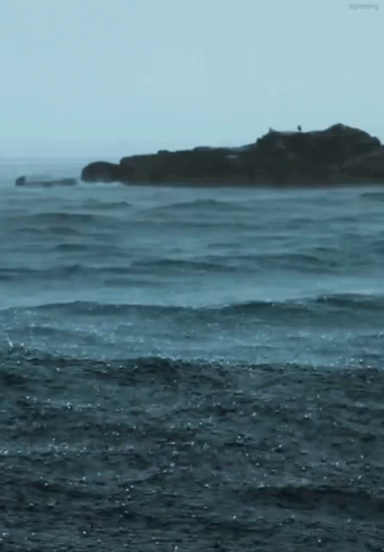two people standing in water near large island in ocean