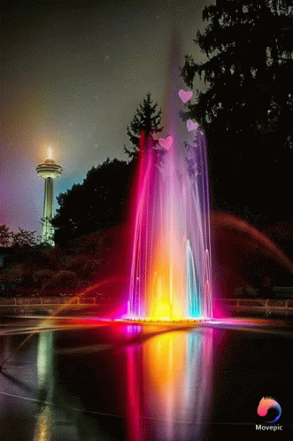 a colorful light fountain in front of a lake with trees